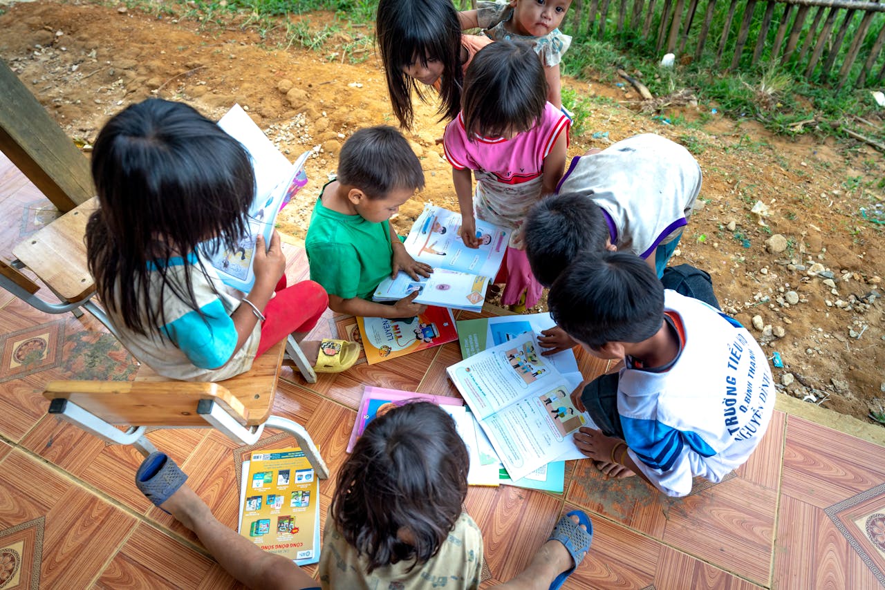 A group of children learning outdoors, sharing and reading educational materials together.